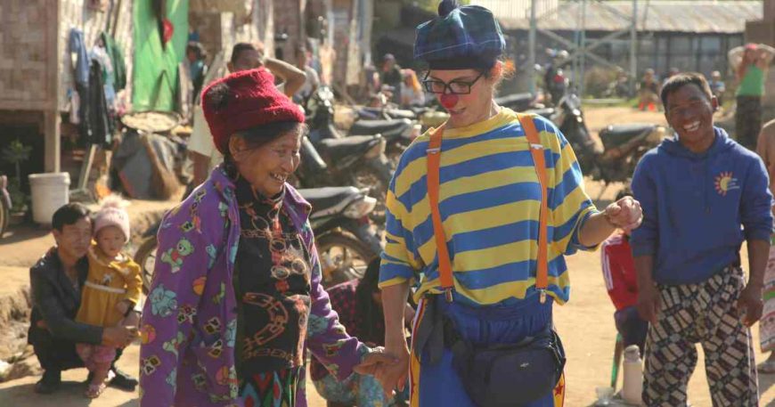 A clown holds the hand of an old woman in Myanmar.