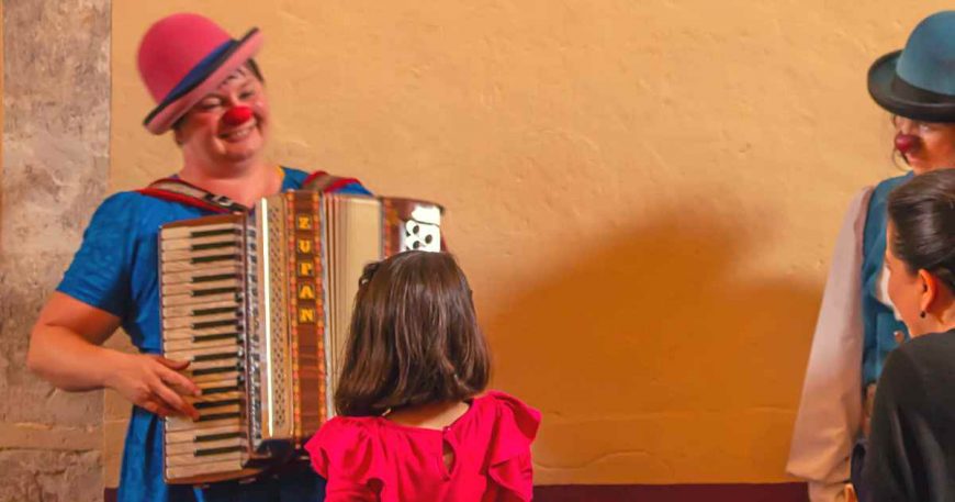 Luz plays the accordion as a small child approaches her, play helps connect clowns and children